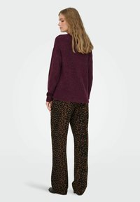 Dunkelburgunderfarbener Pullover mit lockerer Passform und Strickstruktur, kombiniert mit braunen Hose im Leopardenmuster mit weitem Bein. Weicher Stoff, entspannte Silhouette.