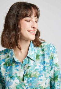 Blouse florale en coton doux. Elle présente un motif aquarelle bleu et vert, un col boutonné et deux petits boutons à l'avant.