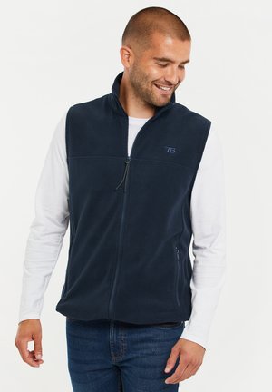 Navy fleece vest with a high collar, front zipper, and side pockets. Features a slight sheen and embroidered logo on the chest.