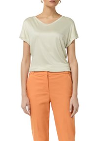 Jasnozielona bluzka z krótkim rękawem w serek, wykonana z miękkiego materiału, w połączeniu z pomarańczowymi spodniami o dopasowanym kroju, charakteryzującymi się czystym cięciem i luźnym dopasowaniem.