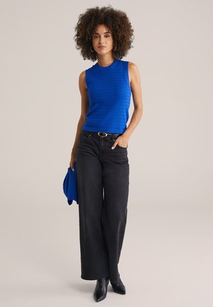 Blå strikket ærmeløs top, sat sammen med højtsiddende sorte vidde jeans og sorte spidse hæle, accessoriseret med en matchende blå sweater.