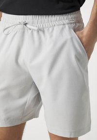 Shorts de sport gris clair en tissu respirant, avec une surface texturée, une taille élastique et des poches latérales.
