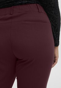 Pantalons bourgogne avec une texture lisse et une taille élastique, comportant une poche arrière unique et une coupe droite.
