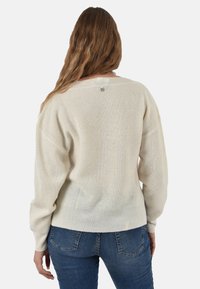 Maglione oversize color crema con texture a coste, scollo ampio e spalle leggermente scese, abbinato a jeans blu.