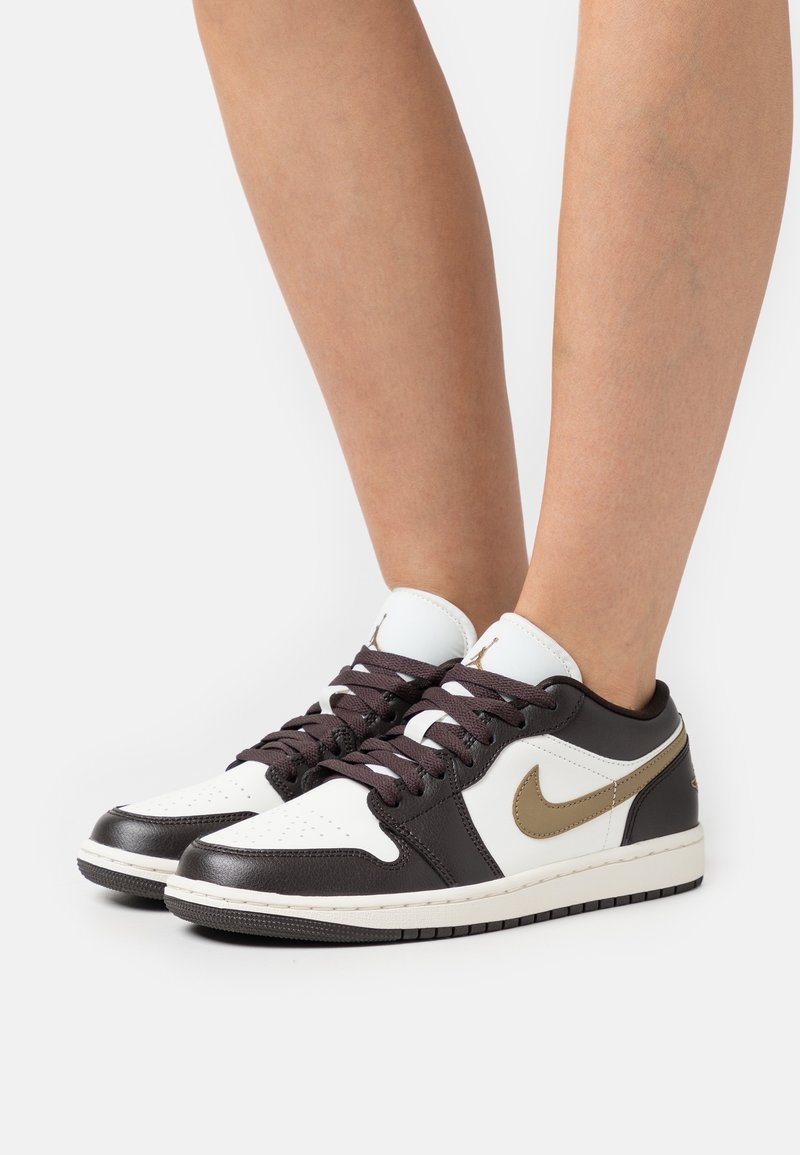 Nike nízké tenisky s bílým svrškem a hnědými akcenty, texturovanou kůží a zlatým logem Swoosh. Ucelený design doplňují tmavě hnědé šňůrky.