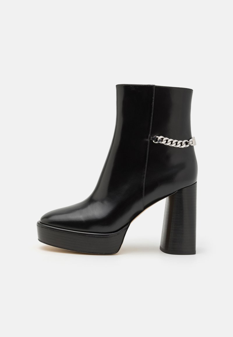Bottine noire en cuir verni avec une plateforme épaisse et un haut talon bloc. Caractérisée par un accent en chaîne argentée sur le côté. Texture lisse.