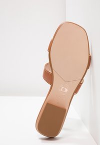 Semelle d'une sandale en cuir marron avec une prise de talon texturée, coutures visibles et logo embossé près de la zone de la voûte plantaire.