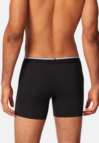 Schwarze Boxershorts mit enganliegendem Schnitt, aus einem glatten Material gefertigt. Merkmale einen grauen elastischen Bund und minimale Nähdetails.