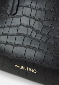 Svart läderhandväska med krokodilpr Präglad textur, sömnadsdetaljer och en guldfärgad "VALENTINO" logotyp accenter.