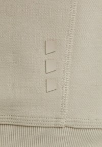 Il tessuto beige chiaro presenta una texture a coste con tre piccoli accenti in pelle angolari attaccati verticalmente. Sono visibili bordi ben cuciti.