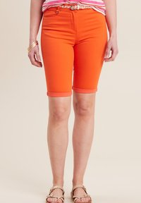 Shorts en denim orange de type bermuda avec des revers, taille haute et poches fonctionnelles, associés à une chemise rayée et des sandales.