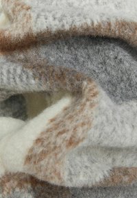 Szalik z mieszanki wełny o teksturowanej, miękkiej powierzchni. Kolory obejmują szary, kremowy i jasnobrązowy z subtelnym, falującym wzorem.