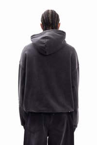 Μαύρο φούτερ με κουκούλα, με χαλαρή εφαρμογή, μαλακή υφή και ρίγες ώμων, σε συνδυασμό με σκούρο παντελόνι, από πίσω όψη.