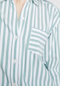 Camicia button-up a righe blu chiaro e bianche con taschino. Realizzata in tessuto traspirante, presenta colletto e vestibilità regolare.