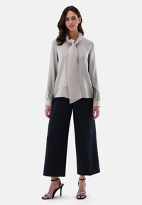 Blusa grigia chiara con un nodo al collo, maniche lunghe e polsini elasticizzati abbinata a pantaloni larghi blu navy. Modella indossa tacchi neri.