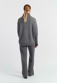 Maglione grigio a maglia con collo alto e vestibilità morbida, abbinato a pantaloni larghi grigi coordinati. Texture morbida, design accogliente, dettagli minimi.