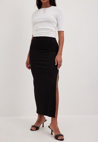 Top blanco de manga corta con detalle acanalado y silueta ajustada, combinado con una falda midi negra acanalada con aberturas laterales, llevado con sandalias negras de tacón.