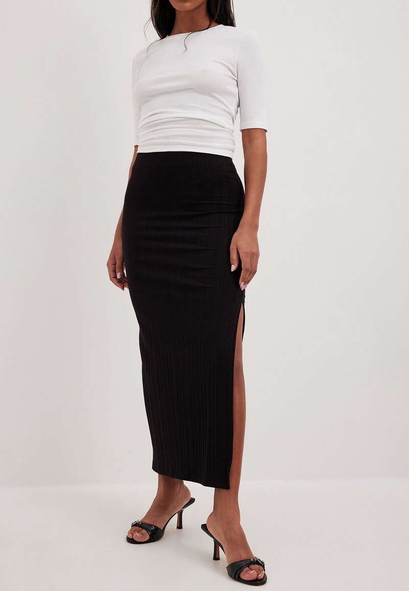 Top blanco de manga corta con detalle acanalado y silueta ajustada, combinado con una falda midi negra acanalada con aberturas laterales, llevado con sandalias negras de tacón.