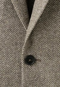 Vlněná tkanina s keprovým vzorem v hnědé a krémové barvě, s černým knoflíkem na klopě.