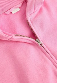 Veste en polaire rose à zip argenté, col côtelé et texture intérieure douce, présentant un design sans couture et un minimalisme en matière de marque.