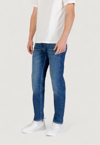 Jeans in denim blu con una vestibilità dritta, leggera scoloritura, design a cinque tasche, indossati con una t-shirt bianca e sneakers bianche.