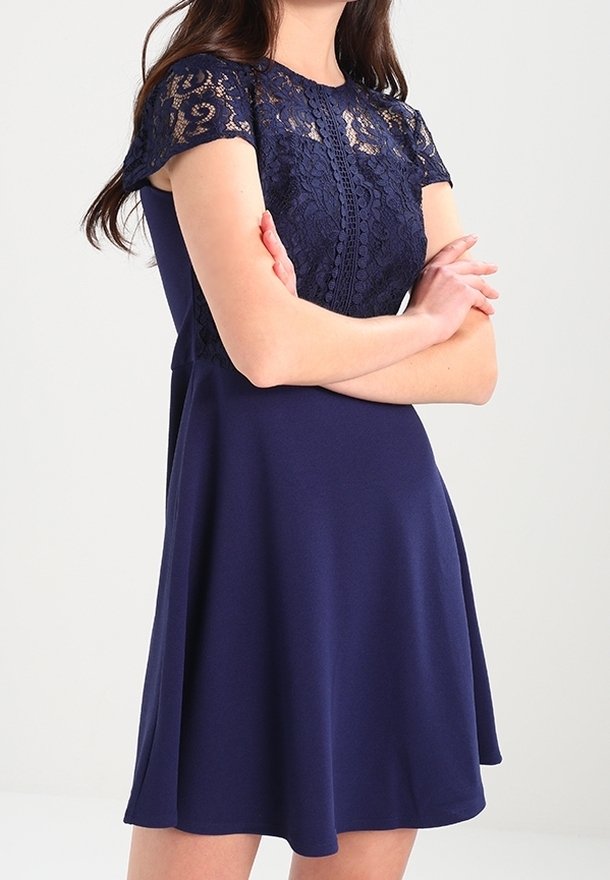 Abito blu navy con corpetto in pizzo a maniche corte, vita aderente e gonna svasata. Tessuto liscio e dettagli di design eleganti.