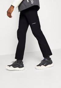 Czarne, zwężane spodnie z zamkami błyskawicznymi przy mankietach i bocznymi kieszeniami. Połączone z masywnymi, szaro-czarnymi sneakersami z fakturowaną cholewką i sznurowadłami.