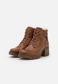 Bottines en cuir marron avec une finition texturée, talon empilé et design à lacets. Doublure douce et languette renforcée visibles.