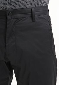 Pantalones negros fabricados con un material suave y ligero. Presentan un cierre de botón, trabillas para el cinturón y bolsillos laterales. Diseño minimalista.