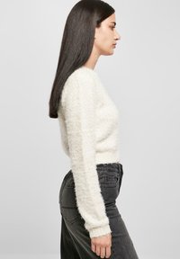Weißer, flauschiger Pullover mit langen Ärmeln, kombiniert mit hoch taillierten schwarzen Jeans. Der Pullover hat eine verkürzte Passform und eine strukturierte Oberfläche.