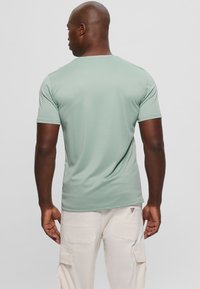 Camisa de manga corta de tela verde suave, con un cuello redondo y una textura suave, combinada con pantalones cargo de color claro.