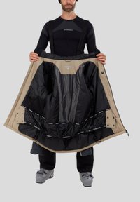 Beige vnější bunda s černou vnitřní podšívkou, s mřížkovým designem, několika kapsami a značkovou nášivkou uprostřed.