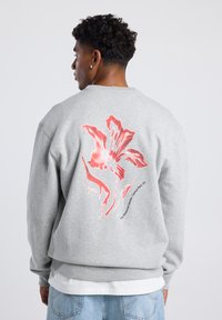 Gray sweatshirt featuring a large red floral print on the back, with text below. Cotton blend material; crew neckline and relaxed fit.