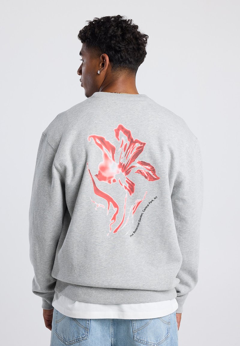 Gray sweatshirt featuring a large red floral print on the back, with text below. Cotton blend material; crew neckline and relaxed fit.