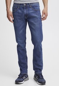 Jeans de mezclilla azul oscuro con corte recto, cinco bolsillos y un ligero desgaste. Combinados con zapatillas negras.
