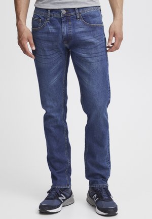 Mørkeblå denimjeans med rett passform, fem lommer og subtil falming. Kombinert med svarte joggesko.
