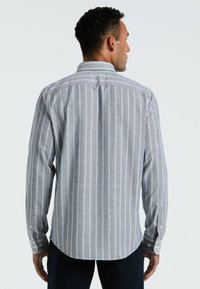 Grijze button-up shirt van stof met verticale witte en lichtblauwe strepen, lange mouwen en een afgeronde onderkant. Voorzien van knopen bij de manchetten.