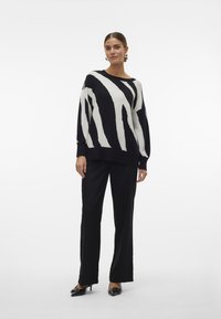 Pullover a righe bianche e nere con vestibilità comoda, maniche lunghe e scollatura ampia, abbinato a pantaloni neri sartoriali e scarpe con punta.