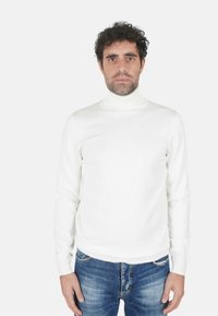 Maglione dolcevita bianco in tessuto lavorato a maglia, con maniche lunghe e design aderente. Indossato con jeans blu strappati.