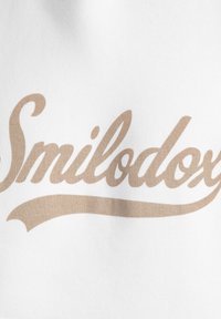Tela blanca con un logotipo en cursiva de color marrón claro que dice "Smilodox", con un adorno decorativo debajo del texto.
