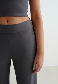 Szürke, magas derekú leggings sima, rugalmas textúrával és logós díszítéssel a derékrészen, amely egy illő crop topsal van párosítva.