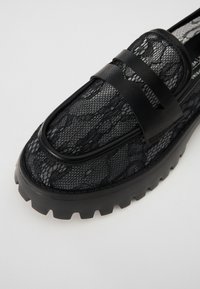 Svarta spetsiga loafers med en texturerad meshovandel, en tjock gummisula med mönster och en horisontell remaccent.