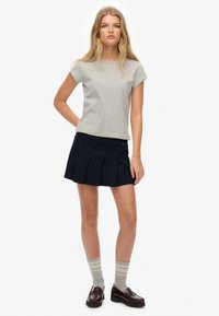 T-shirt in cotone grigio con maniche corte abbinato a una mini gonna nera a righe, calze a strisce grigie e mocassini scuri.