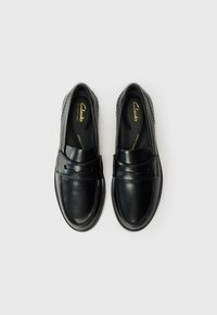 Black leather shoes with a smooth finish, moccasin-style design, decorative stitching, and a low-profile rubber sole. Clarks branding visible inside.