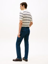 Camisa polo de manga curta, riscada em creme e azul marinho, combinada com jeans escuros de perna reta e sapatos de couro castanho. Vista de trás.