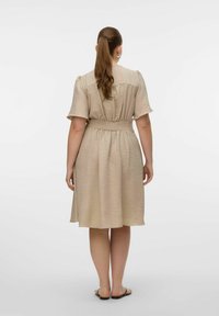 Robe beige à manches courtes, taille élastique et tissu texturé. Silhouette en A tombant jusqu'au milieu du mollet, associée à des sandales plates.