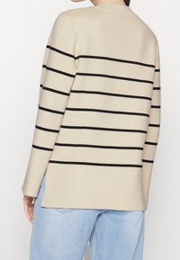 Beige gebreide trui met zwarte horizontale strepen, ronde halslijn en splitjes aan de zijkanten, gecombineerd met lichtblauwe denim. Zachte textuur.