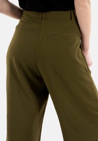 Pantaloni larghi khaki verdi con una finitura testurizzata, caratterizzati da una vita aderente e una tasca posteriore singola. Progettati per un fit rilassato.