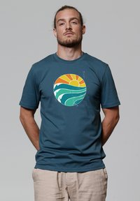 Donkerblauwe korte mouwen t-shirt met een cirkelvormige afbeelding van een oranje zon, groene golven en witte accenten. Zachte stof met een relaxte pasvorm.