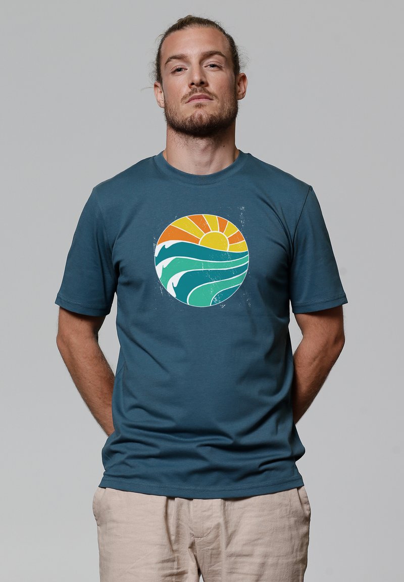 Donkerblauwe korte mouwen t-shirt met een cirkelvormige afbeelding van een oranje zon, groene golven en witte accenten. Zachte stof met een relaxte pasvorm.